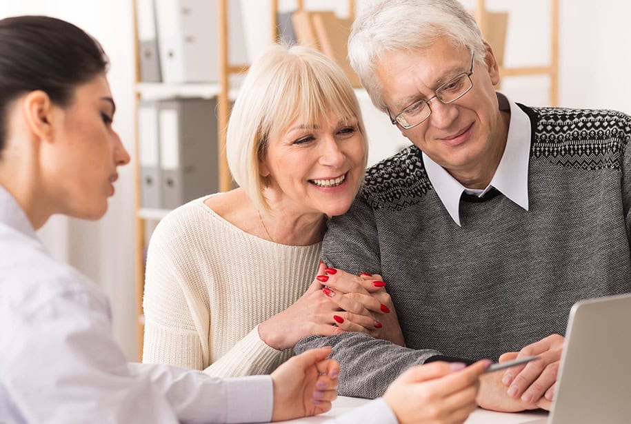 Smiling older couple sitting at a table with a young woman who is pointing to the screen of an open laptop they're looking at