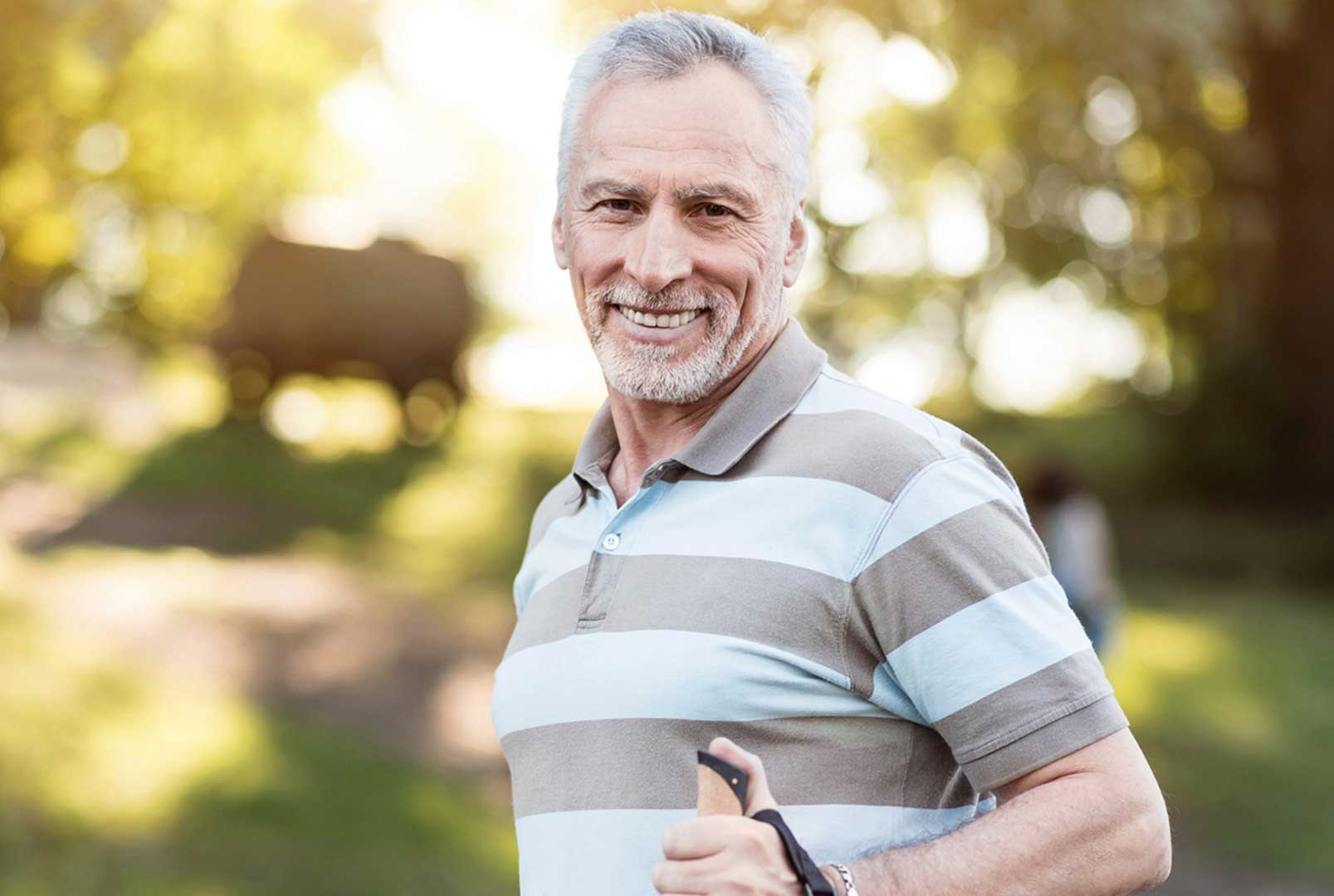 Elderly man wearing a striped t-shirt smiling on a sunny hiking trail